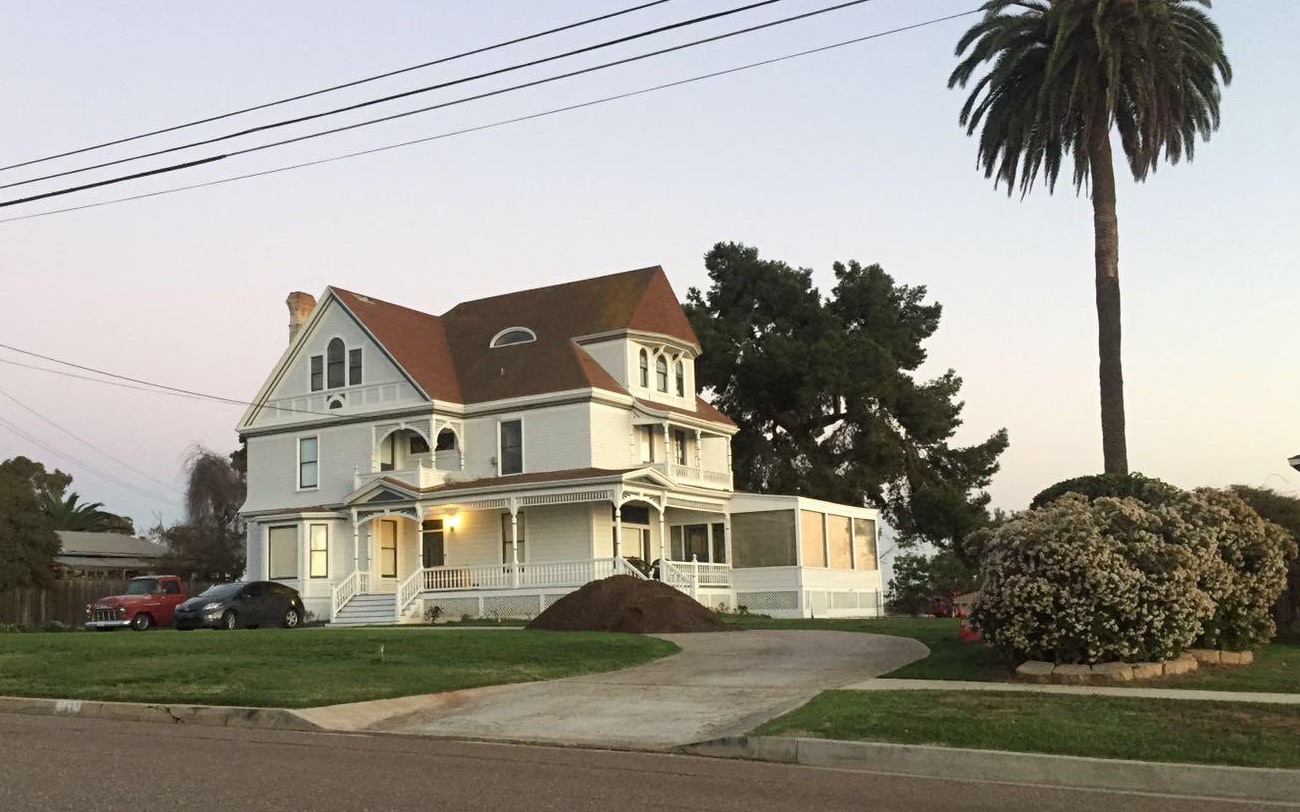 A large white Victorian house at dusk with a palm tree